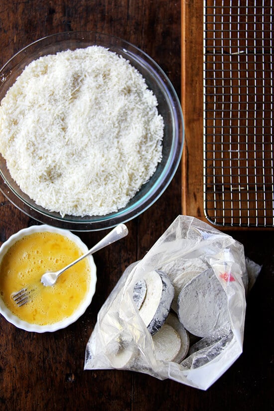 A breading station on a table: bread crumbs, eggs, eggplant tossed with flour.