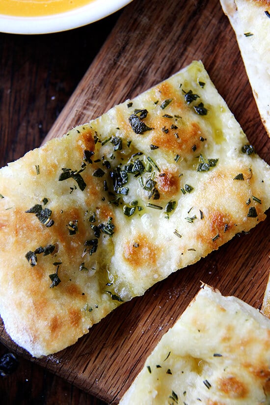 Just-baked herbed flatbread cut into slices on a board. 