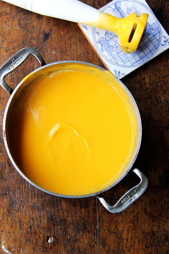 A soup pot with puréed butternut squash soup aside an immersion blender. 