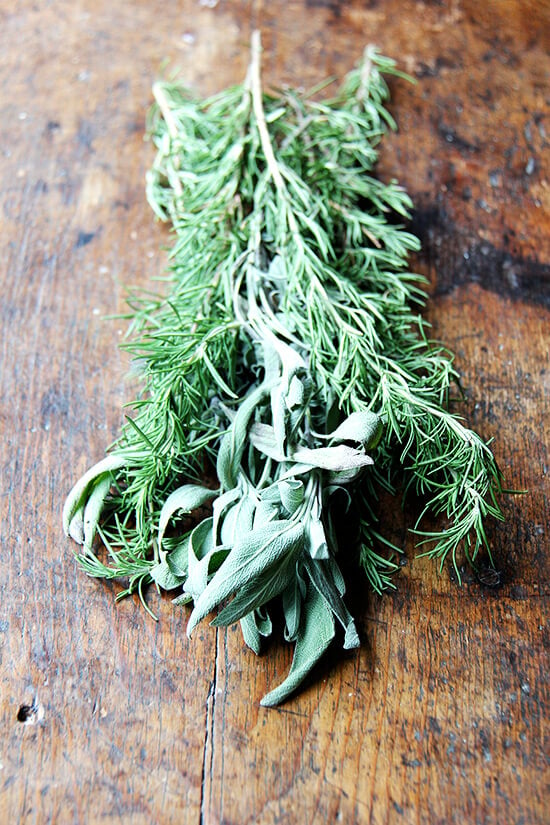 A few sprigs rosemary and sage on a board. 