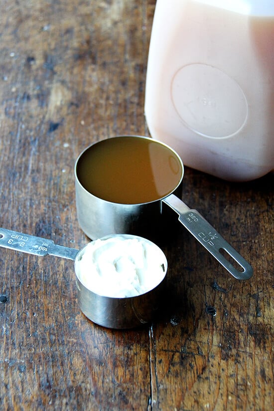 A measuring cup filled with cider aside a cup filled with sour cream.