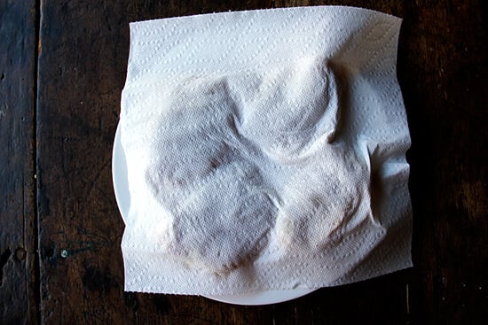 A plate of chicken thighs on a plate covered by a paper towel.