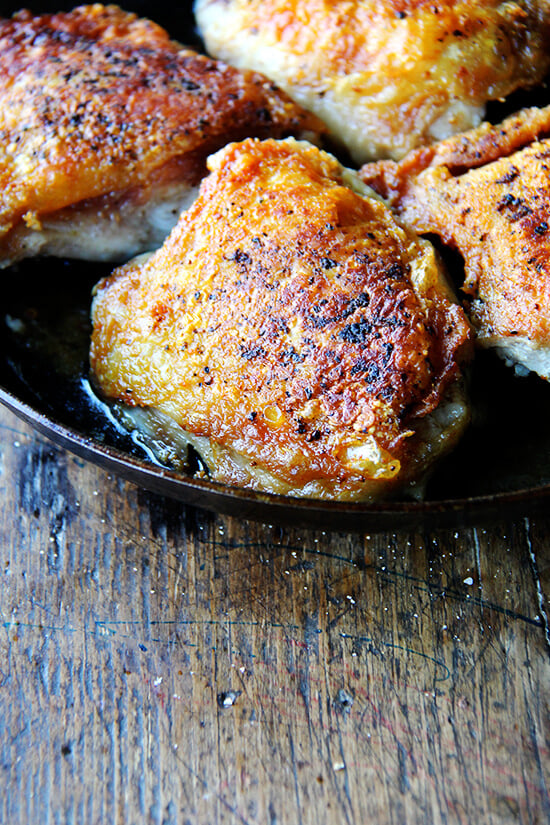 A skillet filled with crispy chicken thighs and preserved lemon.