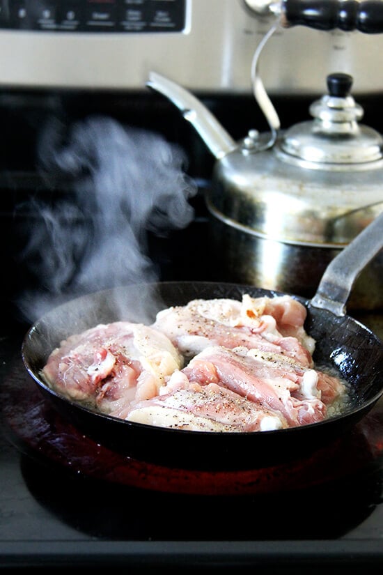 A skillet with chicken thighs cooking on the stovetop.