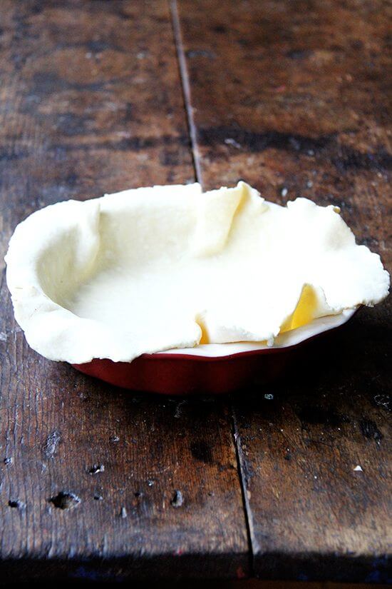 A pie plate filled with a rolled out round of pie dough.