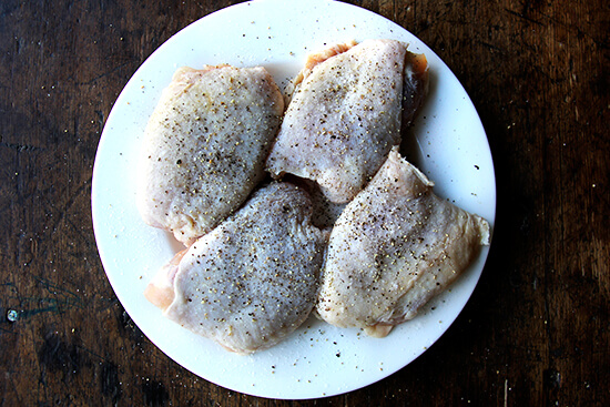 A plate of chicken thighs seasoned with salt and pepper.