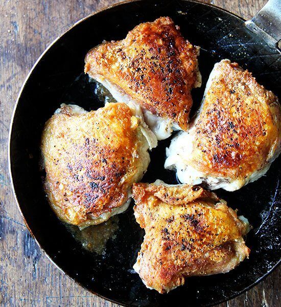 Crispy chicken thighs with preserved lemon in a skillet.
