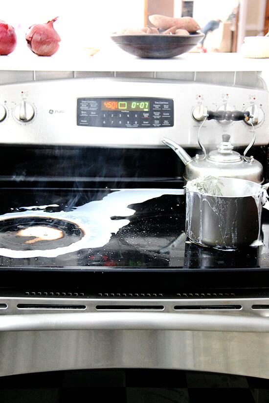 A stovetop with a saucepan that has overflowed with boiling milk that has spilled everywhere. 