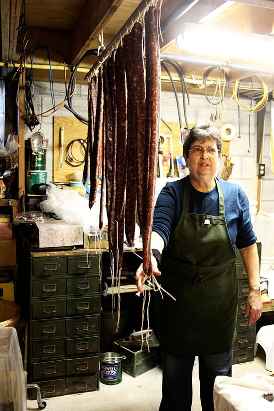 Antonietta standing next to homemade sausage hanging from the ceiling in her basement.