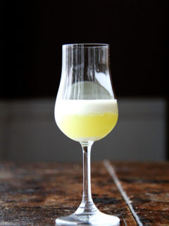 A glass filled with homemade limoncello topped with heavy cream.