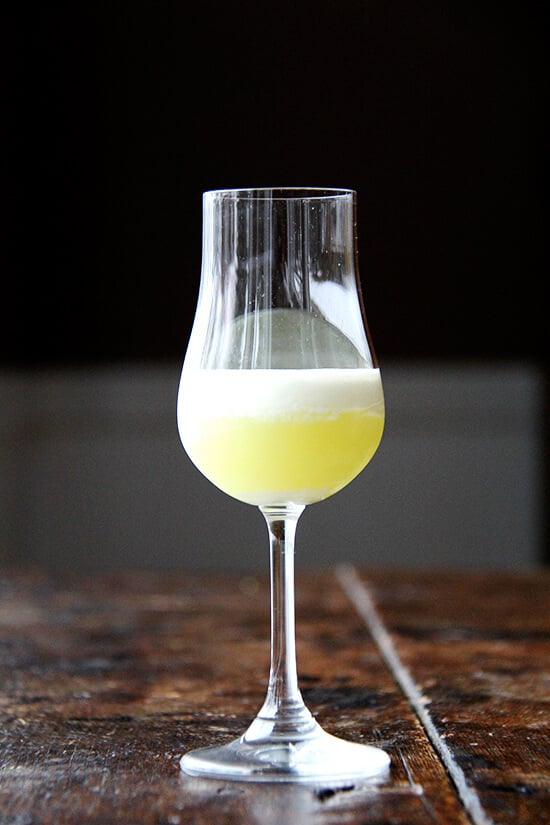 A glass filled with homemade limoncello topped with heavy cream. 