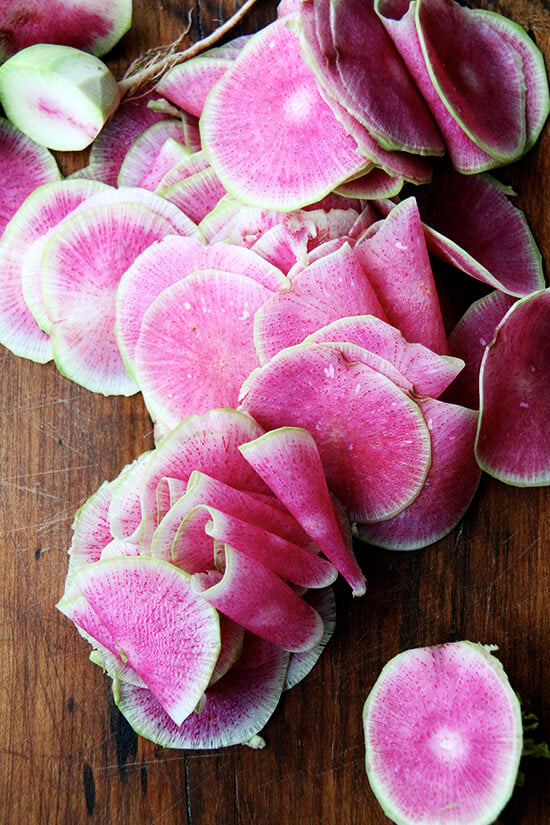 Watermelon radishes, thinly sliced on a board.