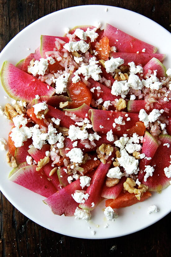 Watermelon radishes on a plate with goat cheese and walnuts and oranges