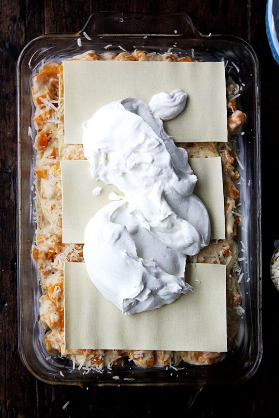 A 9x13-inch pan filled with butternut squash lasagna topped with whipped cream.