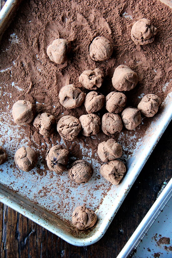 A sheet pan with cocoa powder and truffles rolling in the cocoa powder. 