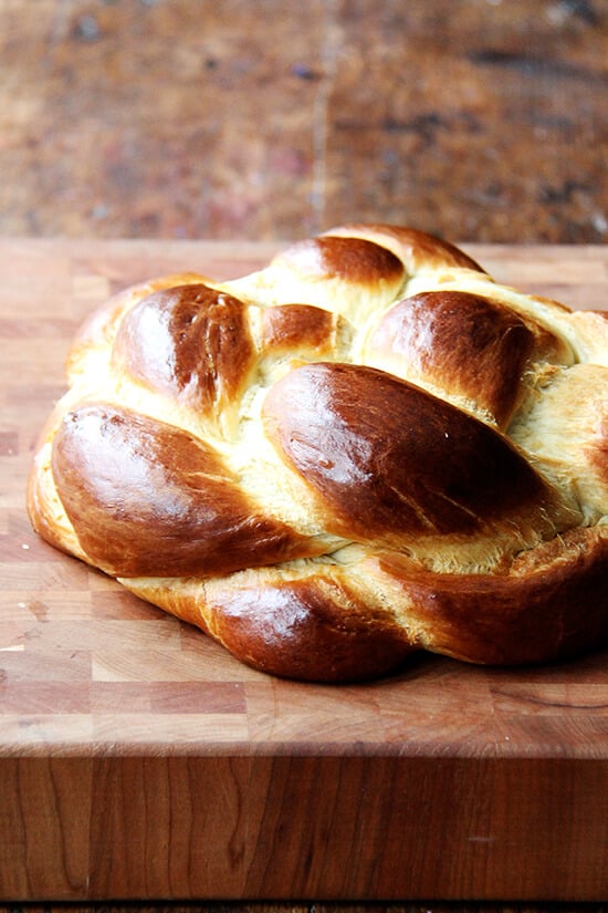 A cutting board with a loaf of challah bread on top. 