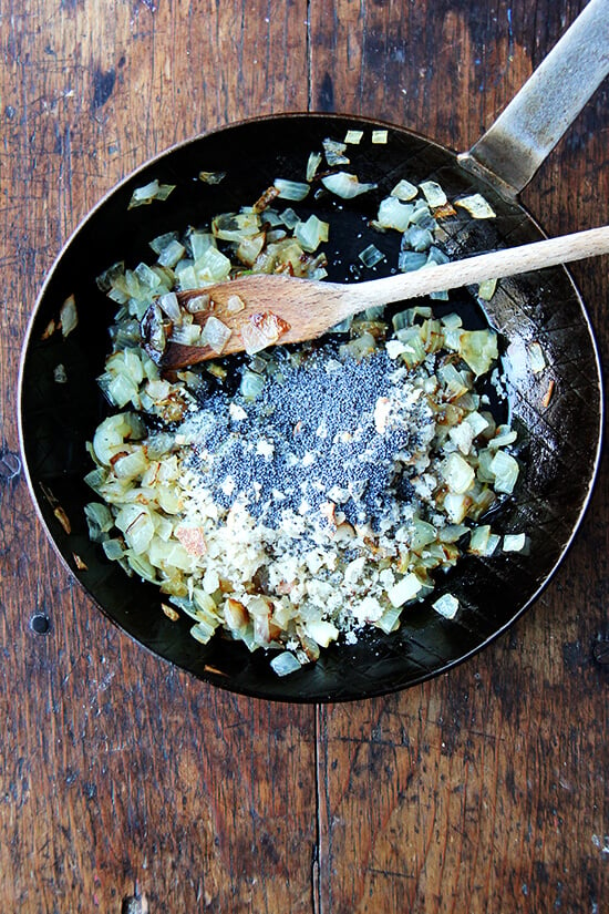 A skillet holding poppy seeds, onions, and bread crumbs.