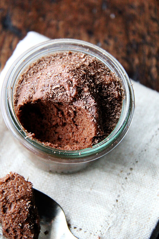 An overhead shot of a small glass of chocolate mousse aside a spoon.