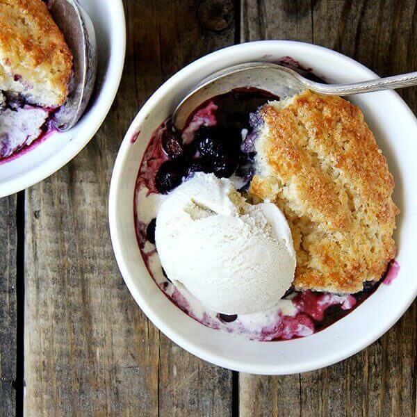 A bowl of blueberry cobbler with ice cream and a spoon.