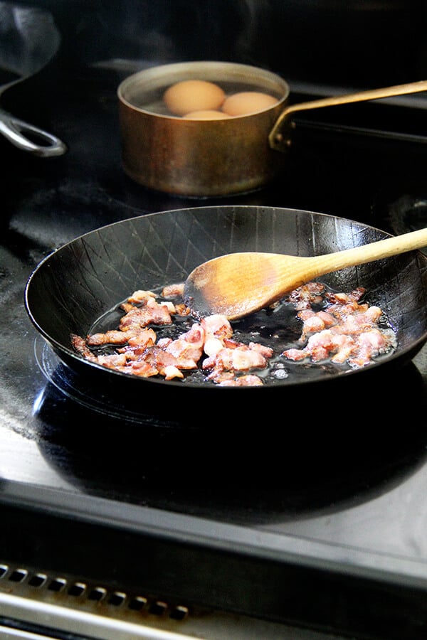 A skillet holding bacon, crisping away.