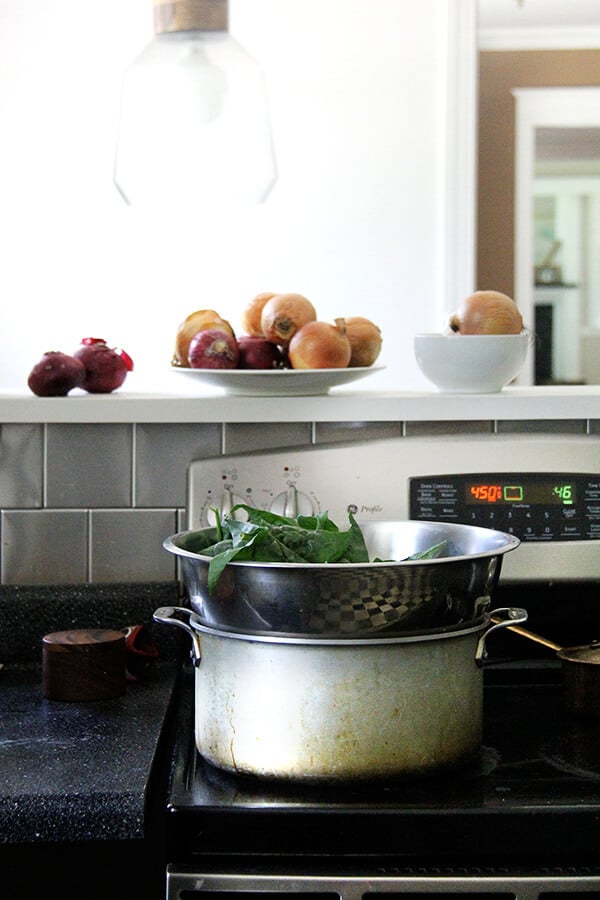 A large pot on a stovetop with a bowl set overtop holding spinach. 