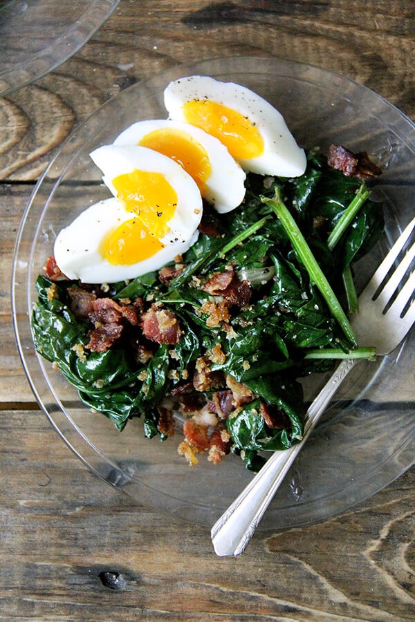 A plate of warm spinach salad with bacon and bread crumbs. 