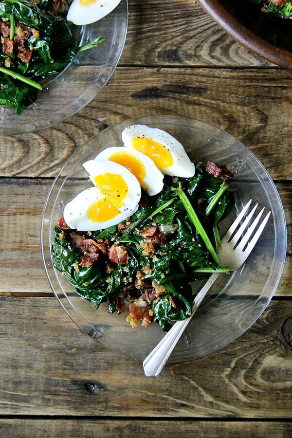 warm spinach salad with bacon and bread crumbs on a plate.