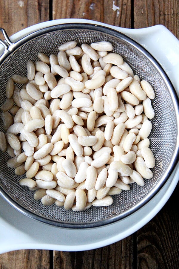 drained soaked white beans in a sieve set over a bowl