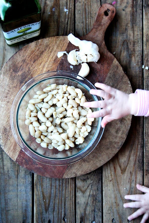 ingredients for stewy white beans on a board: garlic, olive oil, and cooked white beans