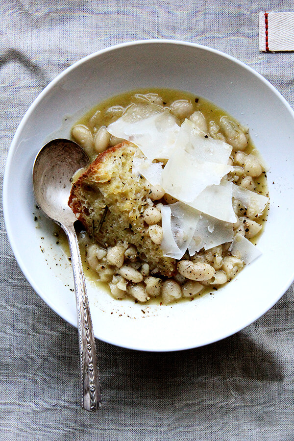 A bowl of stewy white beans with bread and parmesan.