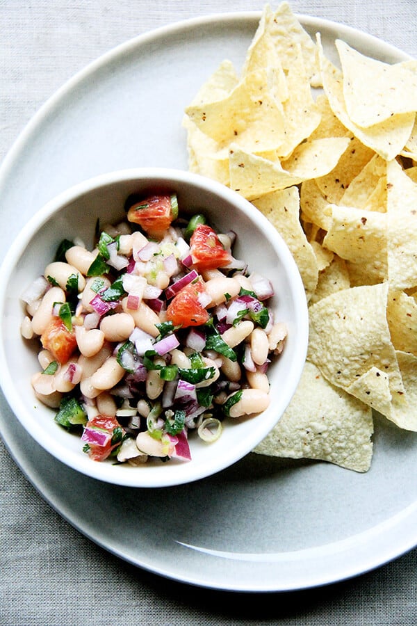 A bowl of white bean salsa aside chips. 