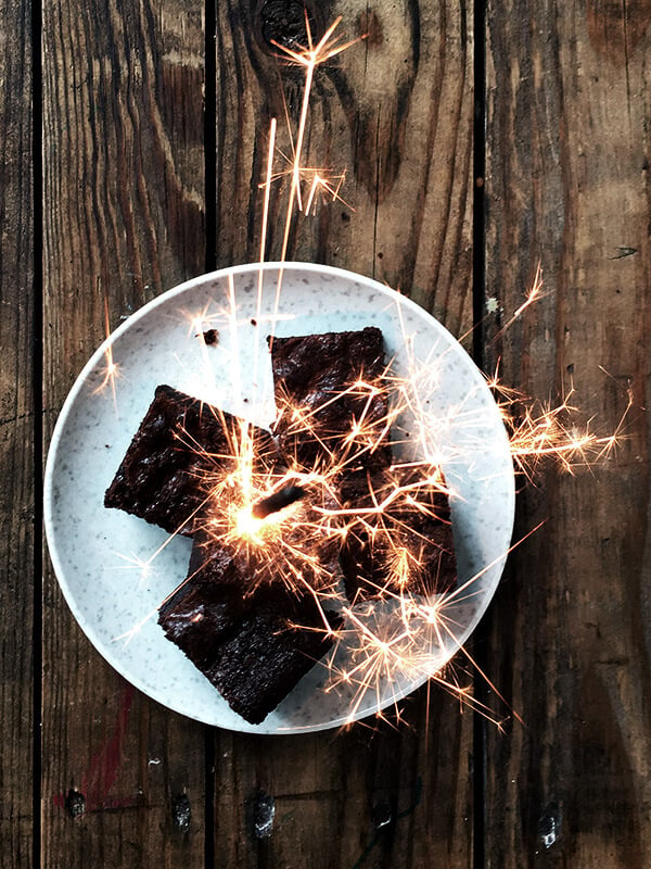 The best ever, rich fudgy brownie recipe on a plate with sparklers lighting off on top of them.