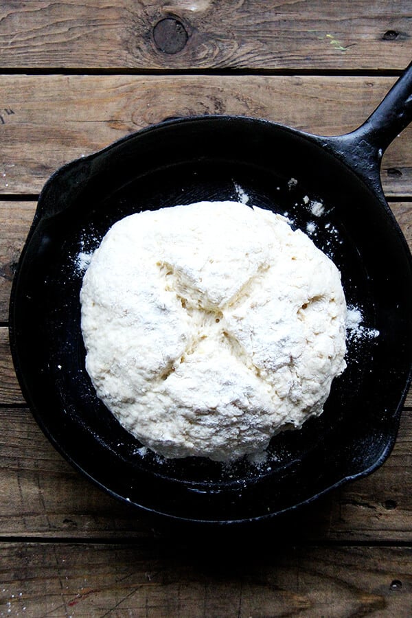 A cast iron skillet of shaped Irish soda bread, scored. 