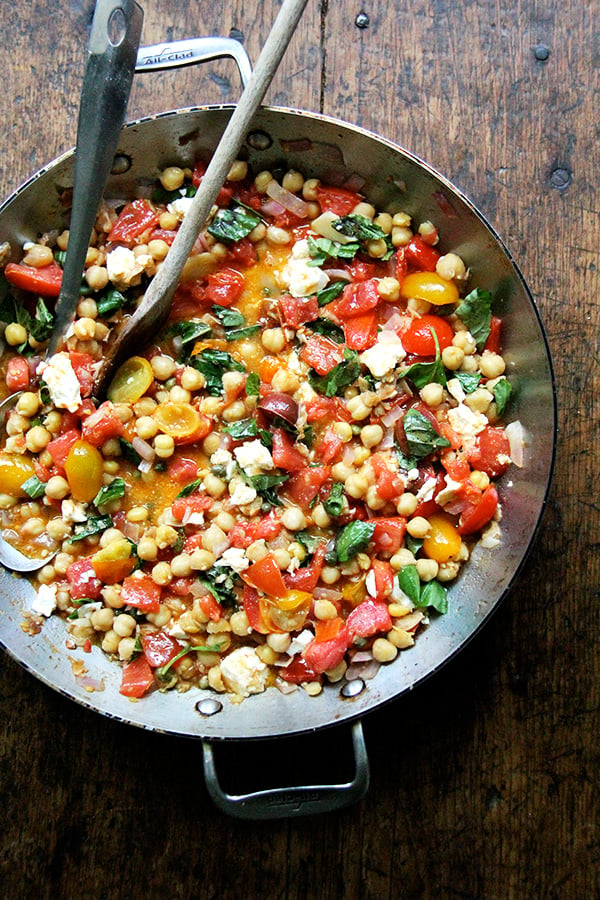 A sauté pan with stewy chickpeas, tomatoes, garlic, and basil. 