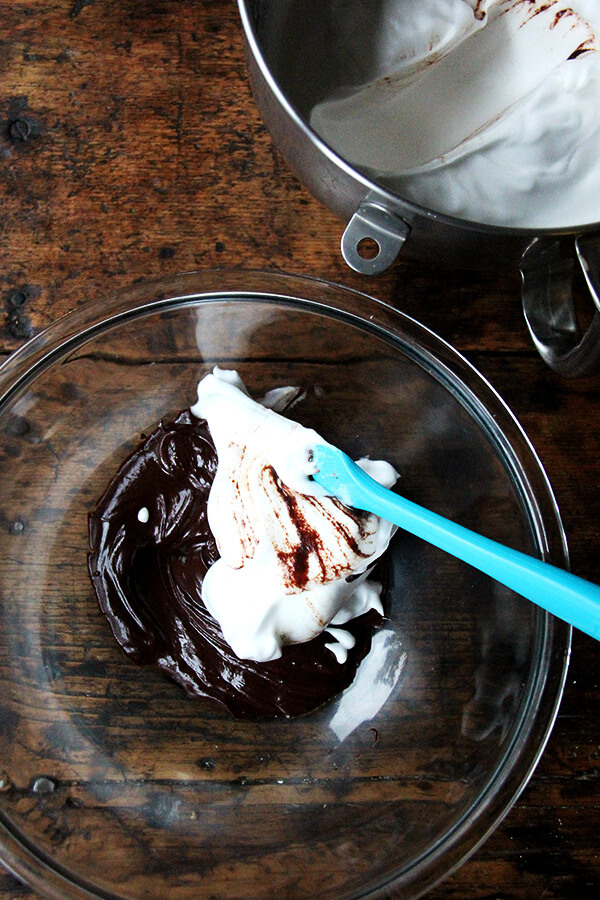 A bowl of melted chocolate and whipped aquafaba being folded together with a spatula. 