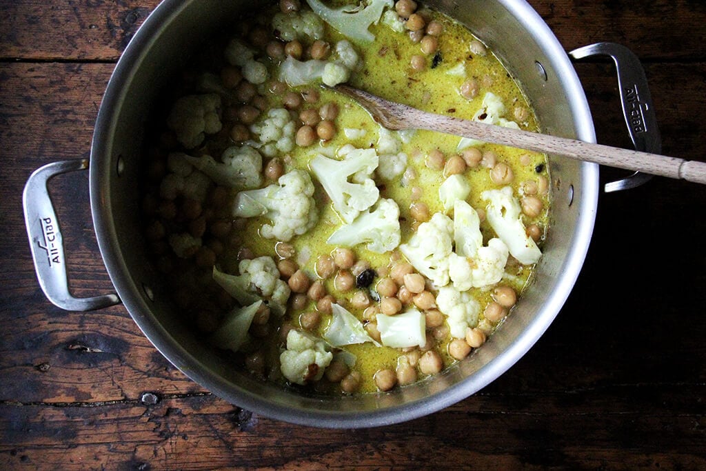A pot with curry spices, cauliflower and chickpeas.