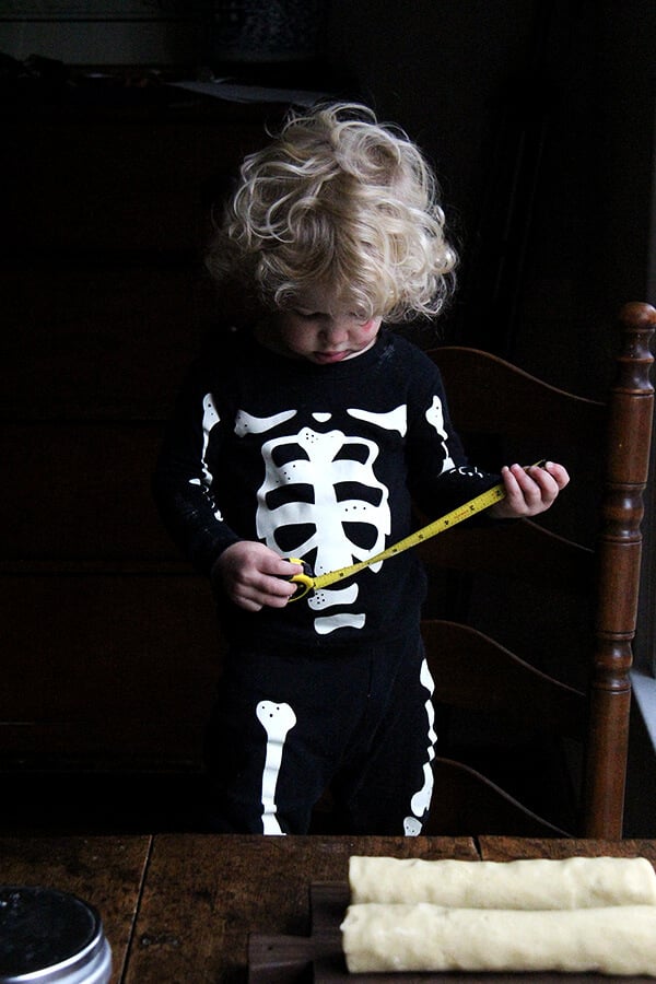 Child dressed in skeleton pjs holding a tape measure. 