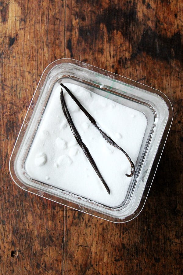 A large container of sugar with two vanilla beans tucked inside.