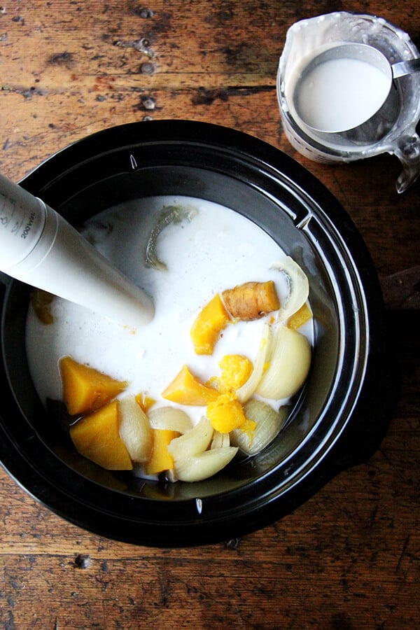 A slow cooker with an immersion blender inserted.