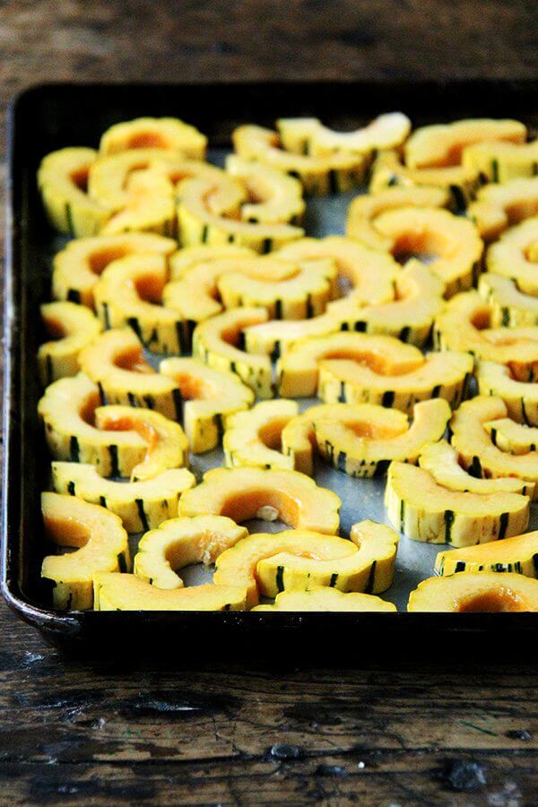 A sheet pan filled with sliced delicata squash, uncooked. 