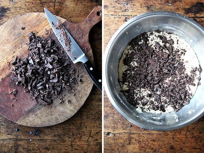 A board with chopped chocolate aside a bowl of dough topped with chopped chocolate. 