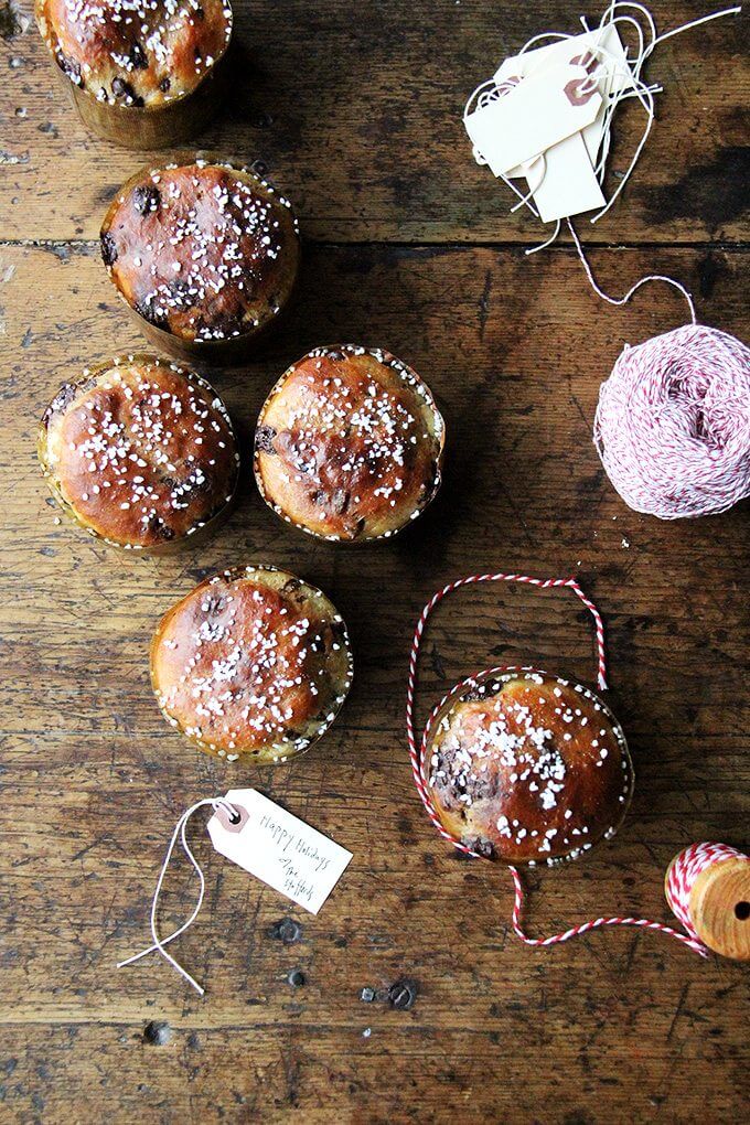 Overhead view of 6 small freshly baked panettone breads aside baker's twines and gift tags