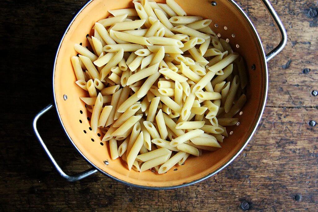 A colander filled with par-cooked penne. 