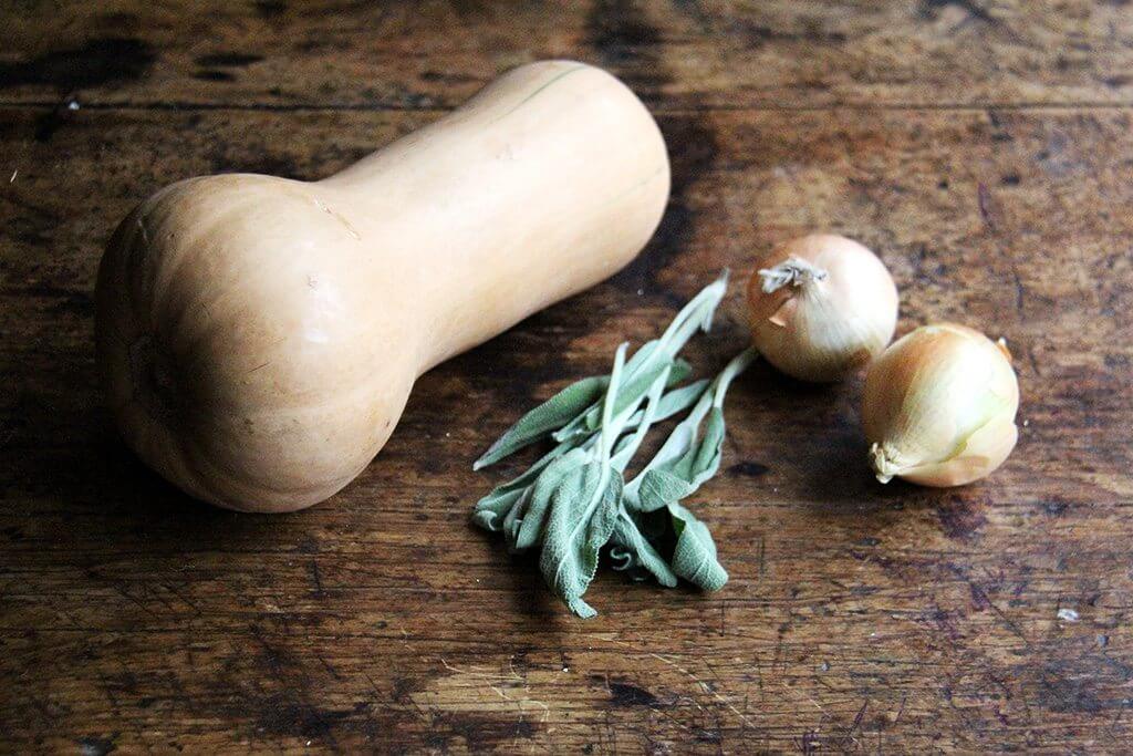 A board with a butternut squash, sage, and onion.