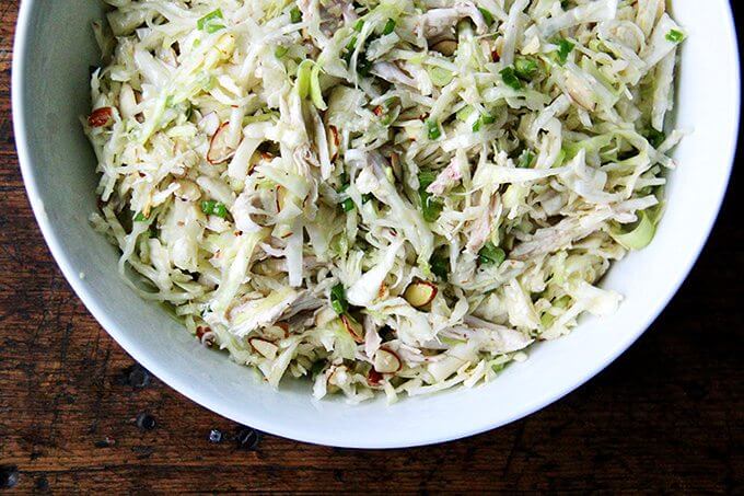 A bowl of chicken and cabbage salad with sesame seeds and almonds.