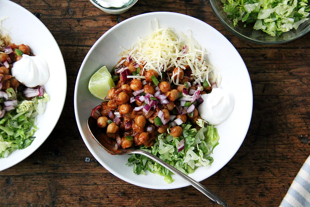 Assembled chickpea taco bowls with lettuce, lime, sour cream, and cheese.