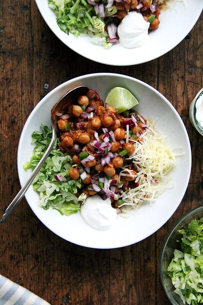 In these chickpea taco bowls, the chickpeas swell with the smoky, spicy, earthy flavors of the chili powder, cumin, crushed tomatoes, and garlic. Sweat the onions, add the seasonings, liquid, and protein, and simmer till flavorful. 