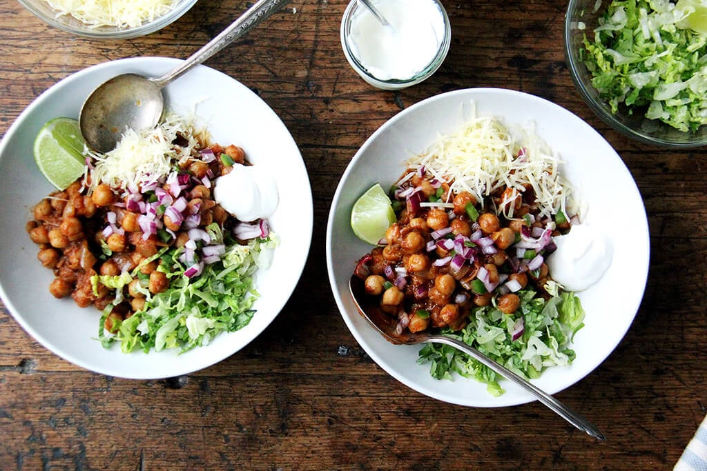 Assembled chickpea taco bowls with lettuce, lime, sour cream, and cheese.