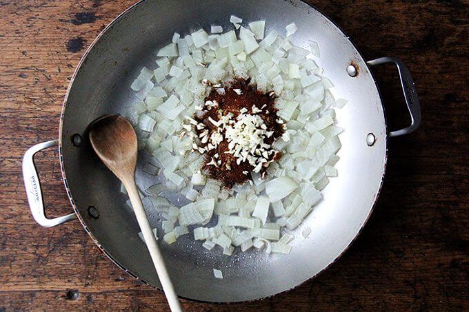 A sauté pan with onions, spices, and garlic. 