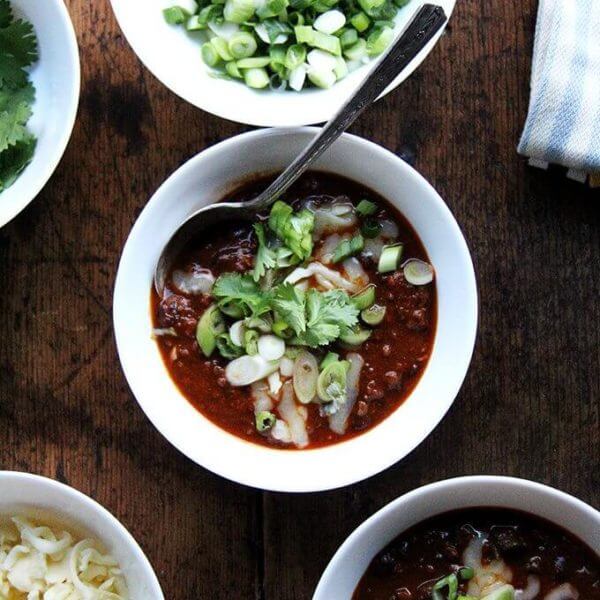 A bowl of weeknight chili topped with scallions and cheddar.